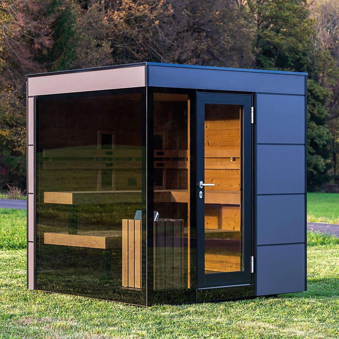 Aussensauna mit grosser Glasfront und dunkler Fassade auf einer Wiese
