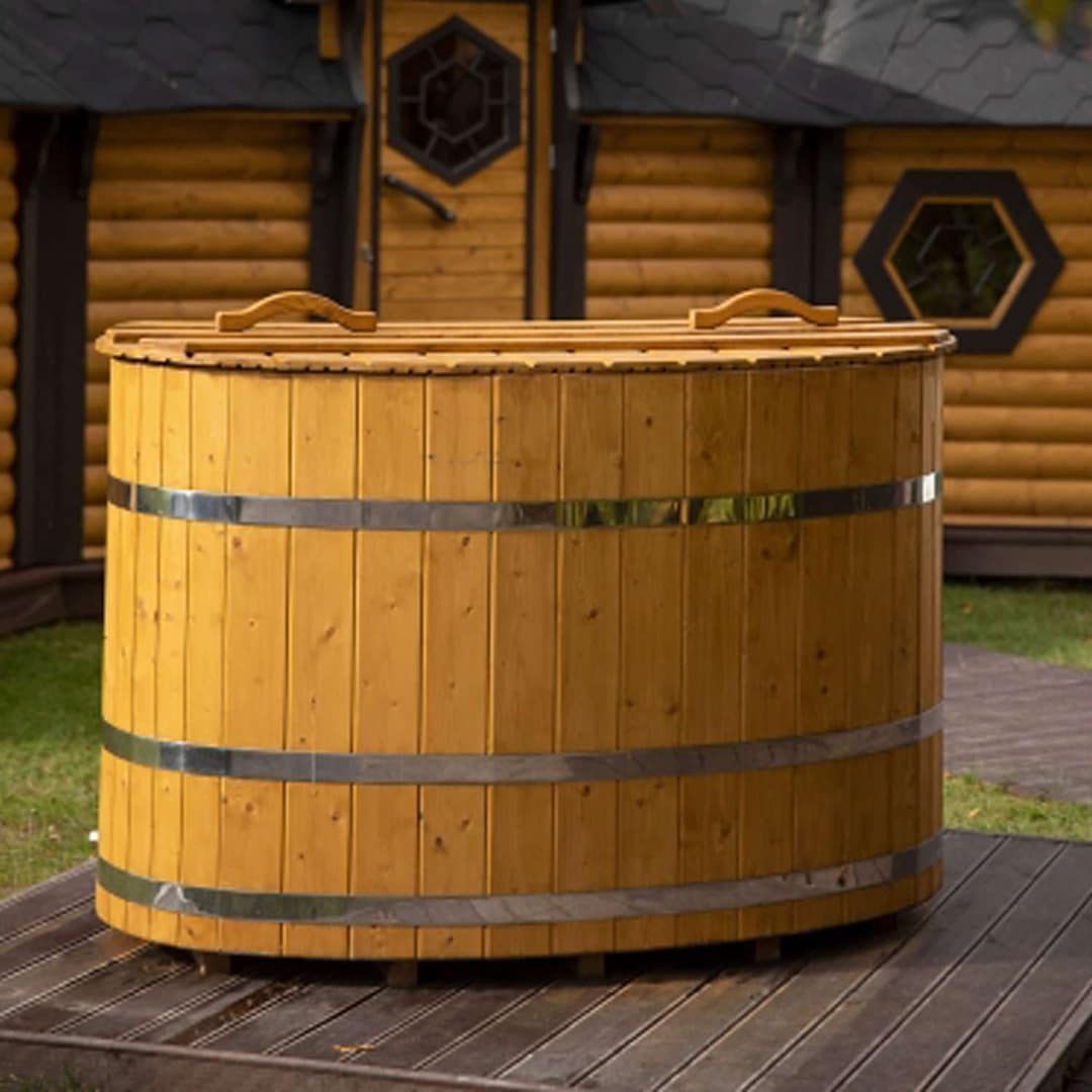 Ovale Holzbadewanne mit Holzdeckel und drei Metallbändern auf einem Holzdeck vor einem Blockhaus