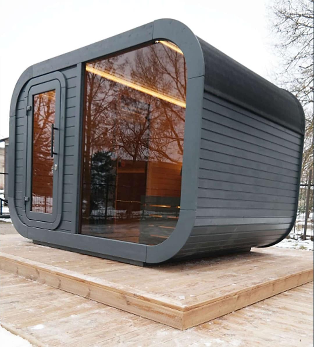 Graue Sauna mit abgerundeten Ecken und grossem Fenster auf einem Holzdeck
