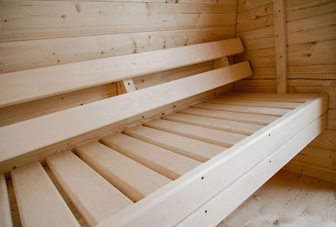 Saunabank aus hellem Holz mit Latten und zweiteiliger Rückenlehne an einer Holzwand