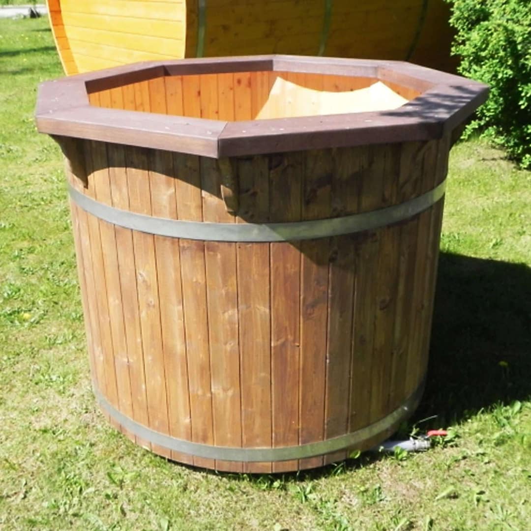 Runder Tauchzuber aus Holz mit dunklem, achteckigem Rand, zwei Metallbändern und Ablassventil auf einer Wiese, dahinter ein Saunafass