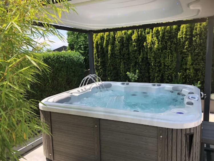 Freistehender Whirlpool mit angehobenem Deckel am Abdeckheber unter einer Pergola