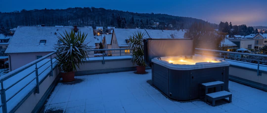 Whirlpool auf einer verschneiten Dachterrasse, aus dem Wasser steigt Dampf